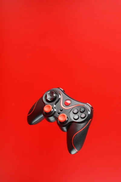 A black joystick game controller hovers isolated on a red background. Interactive entertainment.