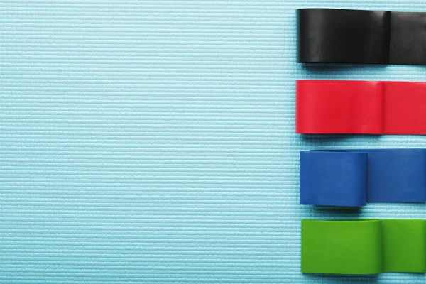 Fitness elastic bands of different colors and loads for sports on a blue background.
