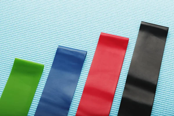 Fitness elastic bands of different colors and loads for sports on a blue background.