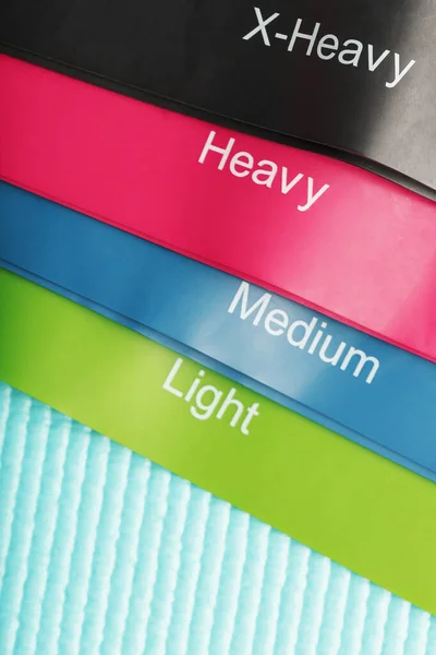 Fitness elastic bands of different colors and loads for sports on a blue background.