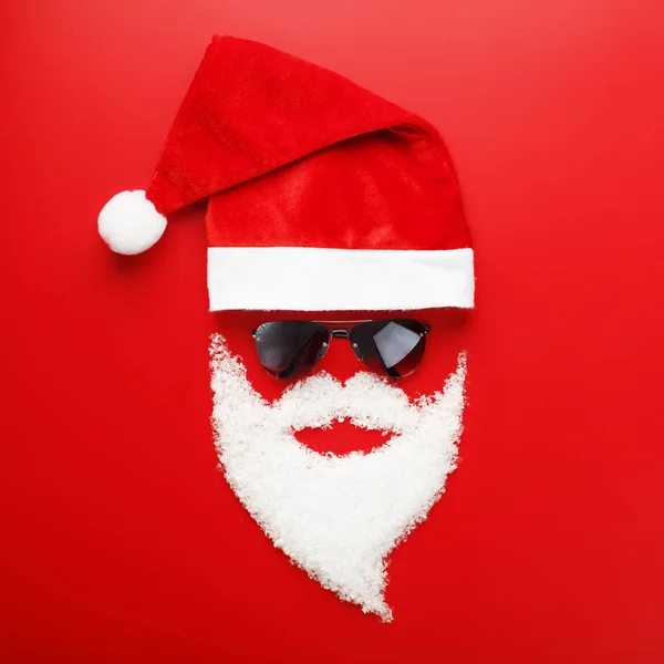 Santa Claus Hat and beard made of snow with black glasses on red background.