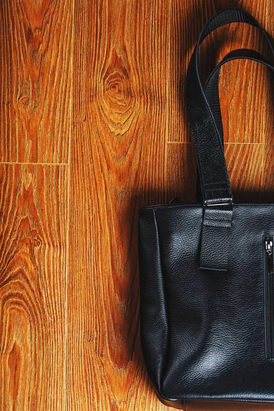 Handmade black leather bag on a wooden background, made of natural material. Design, Hobbies and businesses.