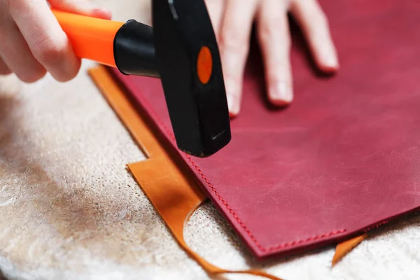 A leather craftsman produces leather goods. He taps the hammer. Handmade work.