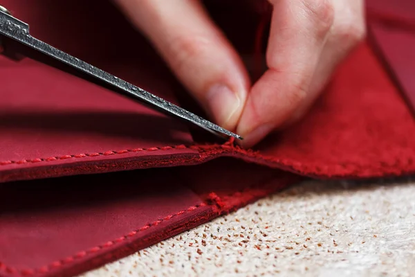 A leather craftsman works with leather. Sews leather goods. Making things handmade. Women\'s hands with a needle, thread, scissors and a blowtorch. Close up