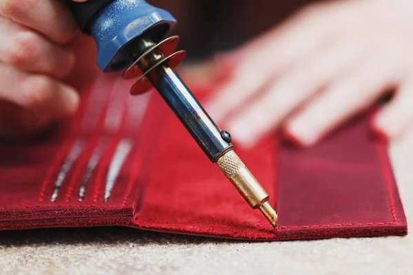 A leather craftsman works with leather. Sews leather goods. Making things handmade. Women\'s hands with a needle, thread, scissors and a blowtorch. Close up