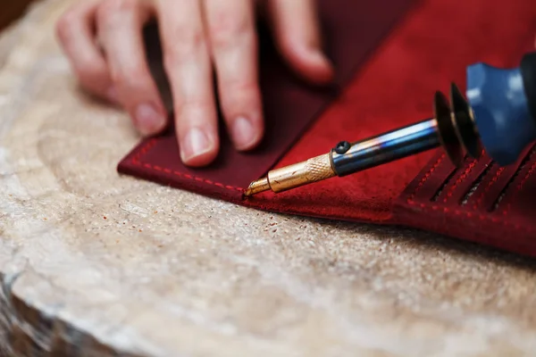 A leather craftsman works with leather. Sews leather goods. Making things handmade. Women\'s hands with a needle, thread, scissors and a blowtorch. Close up
