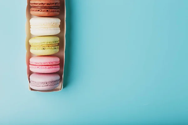 Macaroni cookies of different colors in a white box on a blue background. Free space, close-up shooting from above. The concept of minimalism