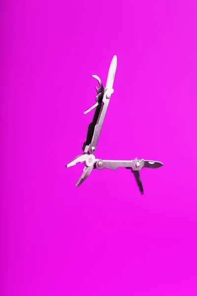 Multitool is a multi-functional tool on a pink background. The concept of an open, flying multi-tool with free space. Clipping path included isolate
