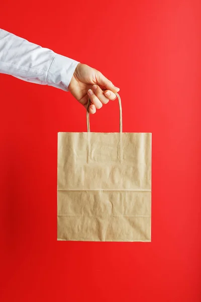 Paper bag at arm\'s length, brown craft bag for takeaway isolated on red background. Packaging template layout with space for copying, advertising.