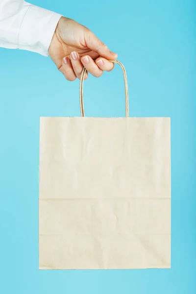 Paper bag at arm\'s length, brown craft bag for takeaway isolated on blue background. Packaging template layout with space for copying, advertising. Concept of assistance, delivery service.