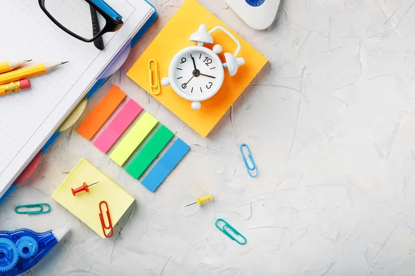 Office supplies lie on a gray table, for working with your own hands at home. The color of the rainbow, pencils, glasses, Notepad and alarm clock remind you of the time. Office. School supplies.