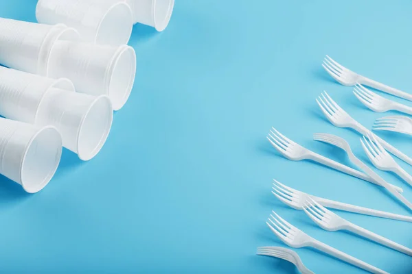 Plastic tableware on a blue background. Disposable forks and glasses with free space. The view from the top