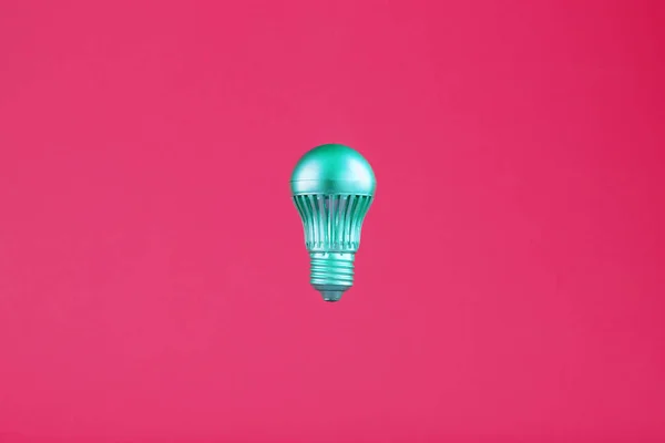 The light bulb hovers in the center of the frame in an isolated space on a pink background. Minimalistic style with conceptual ideas. To be different