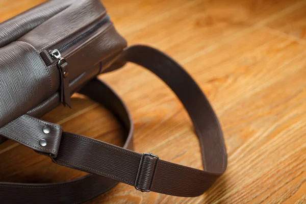 Close-up of the elements of the bag, backpack made of genuine leather with belt buckles and locks. Leather backpack or satchel made of brown leather on a wooden background. Handmade, Studio light.