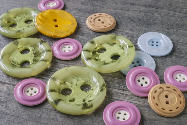 Buttons for clothes - green, yellow, pink, blue, lie on a gray countertop in a chaotic manner.