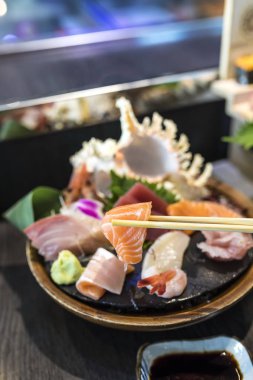 Closeup seçici odak somon balığı Japon restoranında yemek çubukları ile bir dilim chef bar yakınındaki ve arkasında ayarla sashimi bulanık
