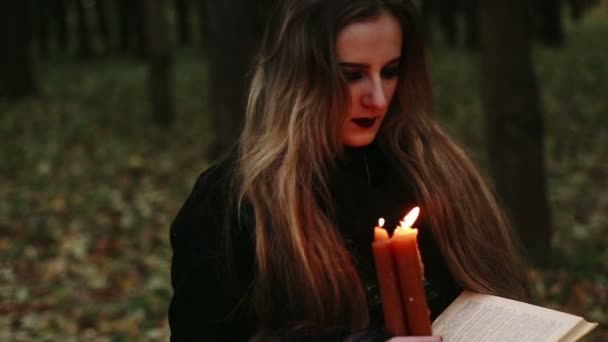 Ведьма с книгой и свечами в лесу — стоковое видео