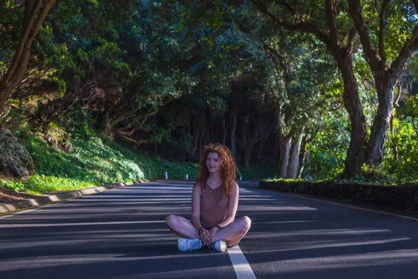 Woman sitting with crossed legs at the road in the forest. Terceira, Azores. Portugal