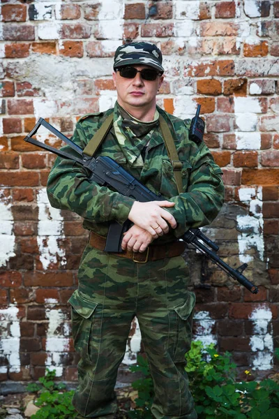 Soldaat of burgerwacht in camouflage met assault rifle Ak-74 blijven in de buurt van bakstenen muur — Stockfoto