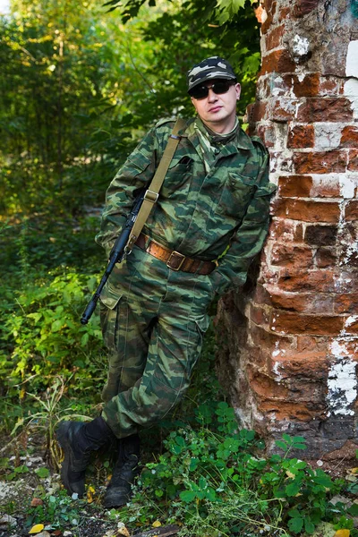 Солдат или милиционер в камуфляже и солнцезащитных очках с автоматом АК-74 остаются у кирпичной стены — стоковое фото