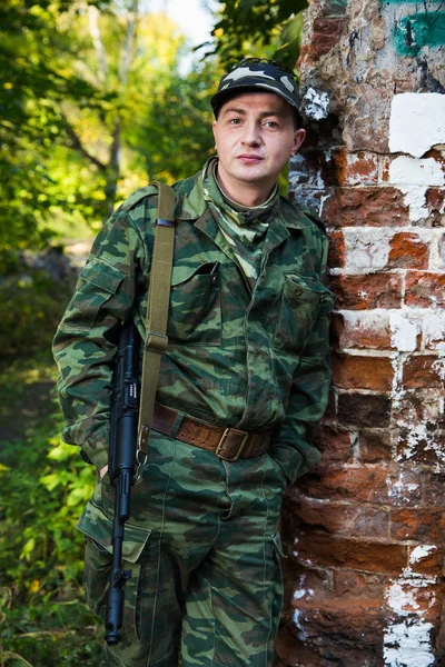 Στρατιώτη ή πολιτοφύλακας σε καμουφλάζ με επιθετικό τουφέκι ΑΚ-74 να μείνετε κοντά σε τοίχο από τούβλα — Φωτογραφία Αρχείου