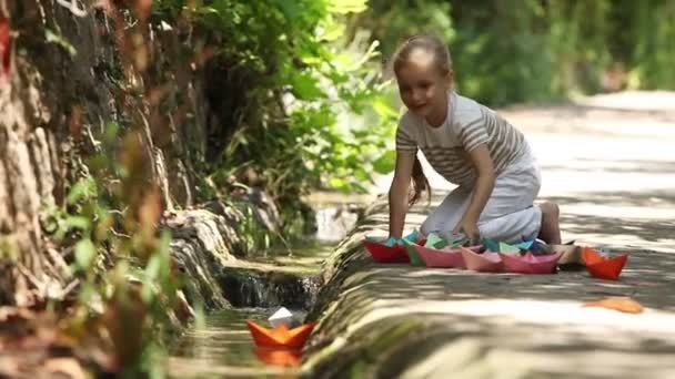 Ragazza seduta vicino al ruscello. Bambino sta lanciando una nave giocattolo galleggiante lungo il torrente — Video Stock