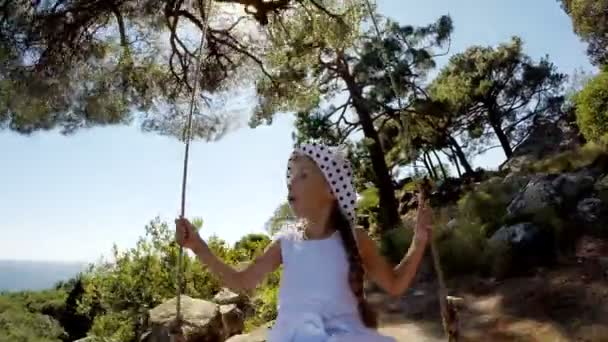 Chica feliz en vestido blanco en un columpio. Ella es feliz y disfruta. Niño sonriendo a la cámara y riendo — Vídeo de stock