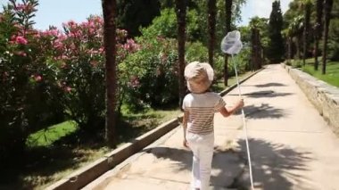 Kız parkta bir kelebek ağı ile yürüyüş. O kameraya gülümseyen ve el sallayarak etrafında dönerek
