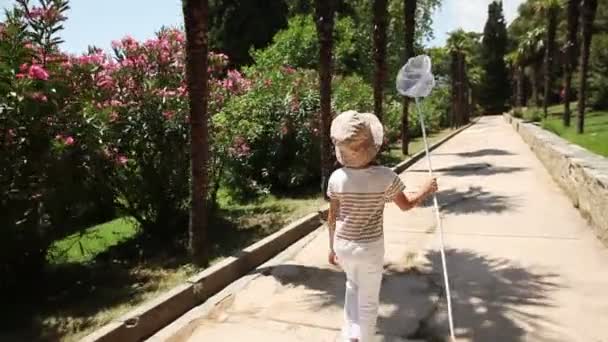 Chica caminando con una red de mariposas en el parque. Se da la vuelta sonriendo a la cámara y saludando con la mano — Vídeo de stock