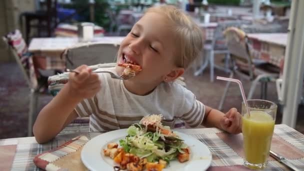 Дівчина їсть креветки та салат у кафе. Дитина дивиться в камеру і посміхається — стокове відео