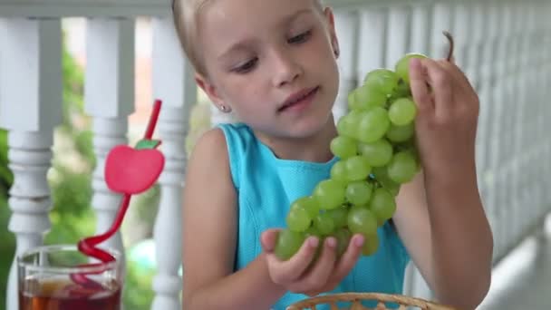 Retrato de uma rapariga com um monte de uvas. A criança olha para a câmera e sorri. Mostra classe. Polegares para cima — Vídeo de Stock