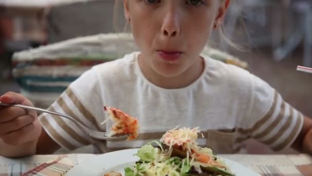 Chica comiendo ensalada de camarones en el café. Niño mirando a la cámara y sonriendo — Vídeo de stock