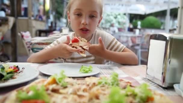 Mädchen isst Pizza im Restaurant und schaut in die Kamera — Stockvideo