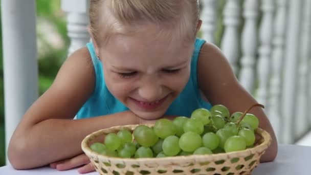 Menina com uma cesta de uvas na mesa mostra classe e sorrindo para a câmera. Polegares para cima. — Vídeo de Stock