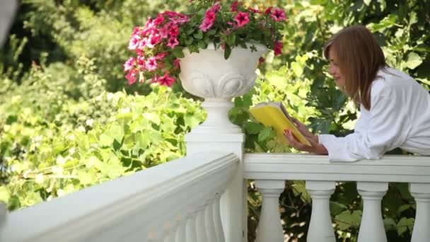 Giovane donna adulta felice in accappatoio mentire e leggere un libro. Guardò la macchina fotografica e sorrise — Video Stock