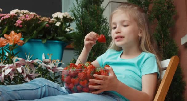 Chica sosteniendo un enorme plato de fresas y comerlo. Mirando la cámara — Vídeos de Stock