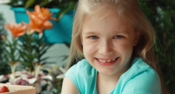 Дитяча дівчинка з жменькою полуниці дивиться на камеру — стокове відео