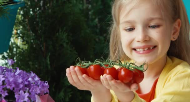 Closeup portrait laughing girl holding cherry tomatoes and invites the viewer — Stock Video