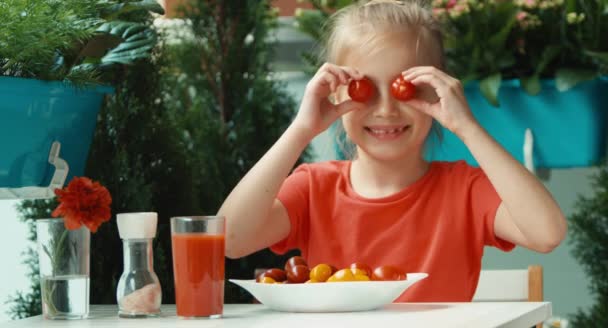 Fille barbote avec des tomates cerises. Au lieu de tomates aux yeux. Regarder et sourire à la caméra — Video