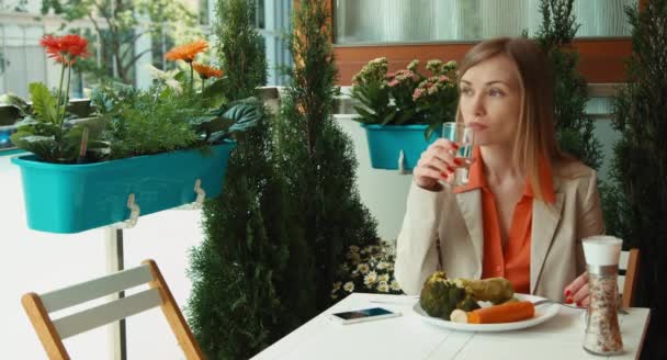 Femme d'affaires boire de l'eau et manger des légumes et regarder la caméra — Video