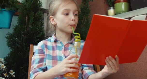 Close up retrato menina lendo um livro e beber suco de cenoura — Vídeo de Stock