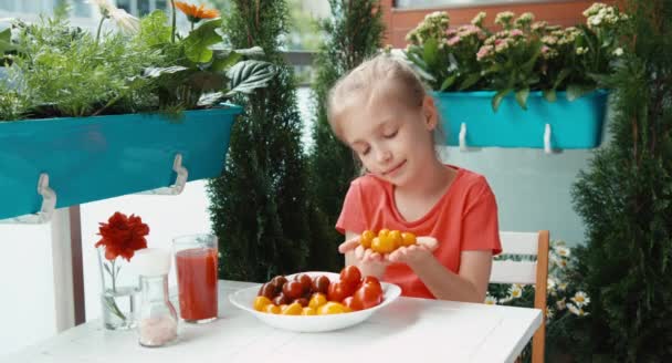 女孩和少量的樱桃番茄。孩子给观众的食物。在相机微笑 — 图库视频影像