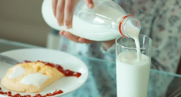 Menina retrato close-up derramando leite em um copo e bebendo. Criança sentada na mesa da cozinha — Vídeo de Stock