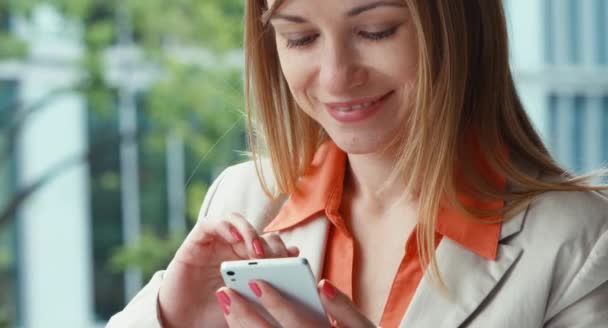 Closeup portrait businesswoman using mobile phone and smiling. She is from the outside and smiling at the camera — Stock Video