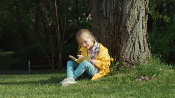 Τον αντίχειρα επάνω. Ok. Παιδί διαβάζοντας ένα βιβλίο καθισμένος κάτω από ένα δέντρο και να βλέπουν τα φωτογραφικών μηχανών — Αρχείο Βίντεο