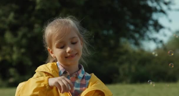 Крупним планом портрет дитини, що дме мильні бульбашки і сміється — стокове відео