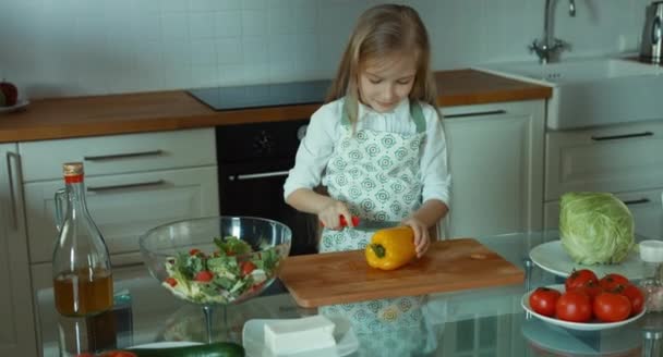Mädchen schneiden Pfeffer. Kinderkoch in der Küche blickt in die Kamera und lächelt — Stockvideo