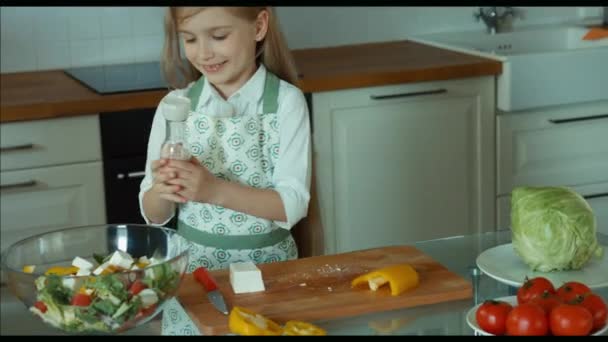 Salada de menina polvilha sal. Chef infantil na cozinha. Zumbido — Vídeo de Stock