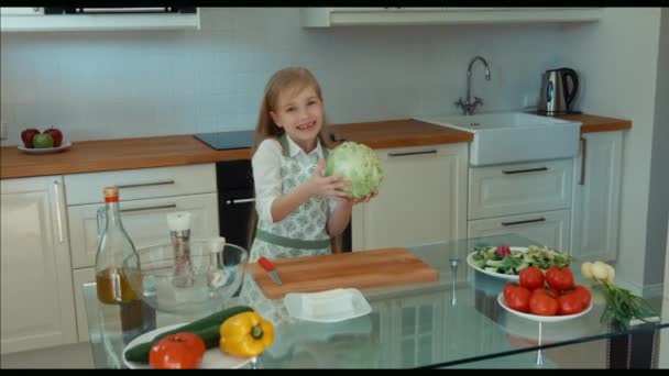 Девушка-повар на кухне держит капусту, смотрит в камеру и смеется. Zooming — стоковое видео