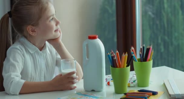 Vorschulmädchen trinkt Milch. Er blickt auf Fenster und Kamera und lächelt. Schwenken. Daumen hoch. ok — Stockvideo